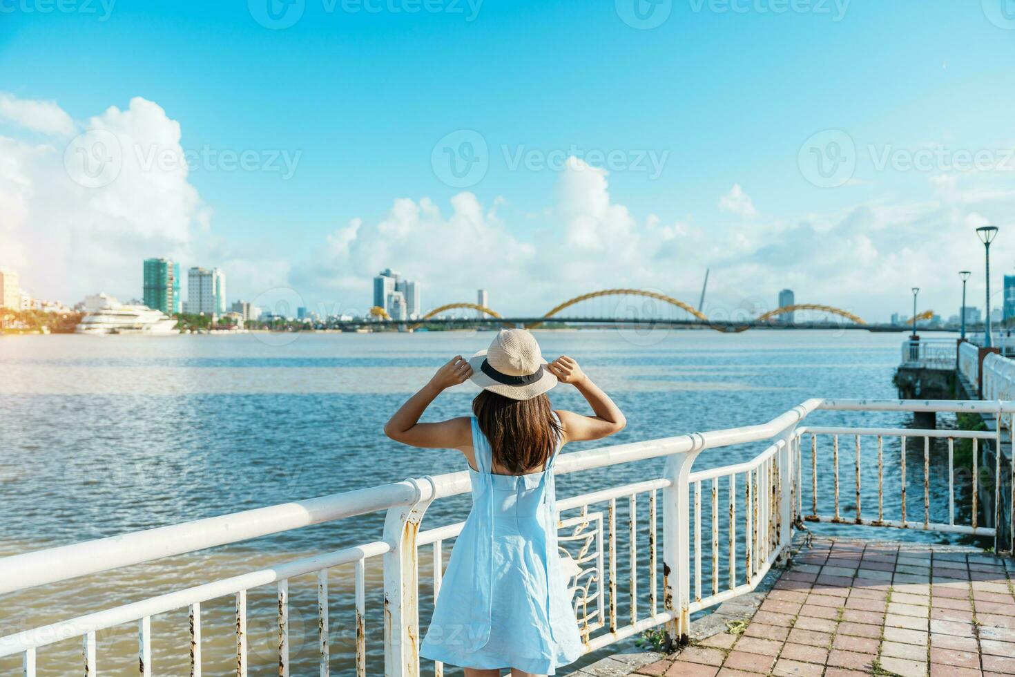 Woman Traveler with blue dress visiting in Da Nang city. Tourist sightseeing the river view with Dragon bridge. Landmark and popular for tourist attraction. Vietnam and Southeast Asia travel concept photo