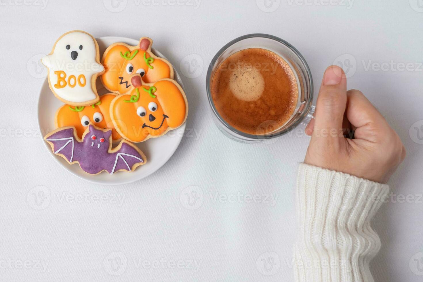 woman hand holding coffee cup during eating funny Halloween Cookies. Happy Halloween day, Trick or Threat, Hello October, fall autumn, Traditional, party and holiday concept photo