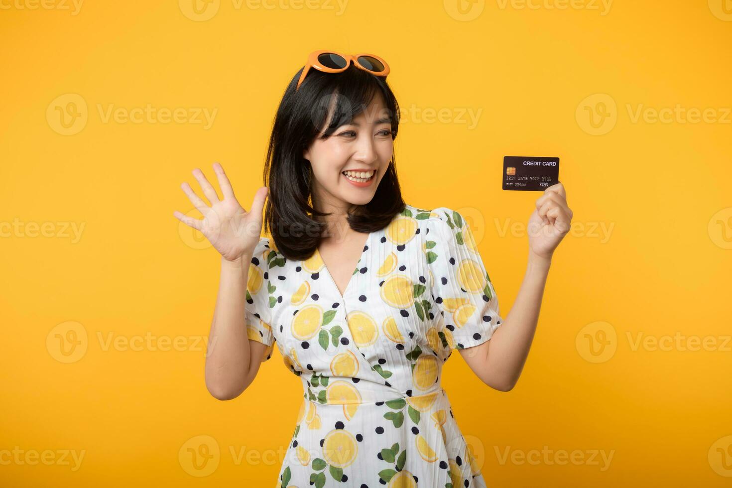 Portrait young asian woman happy smiling in springtime dress showing plastic credit card isolated on yellow background. Pay, money and purchase shopping payment concept. photo