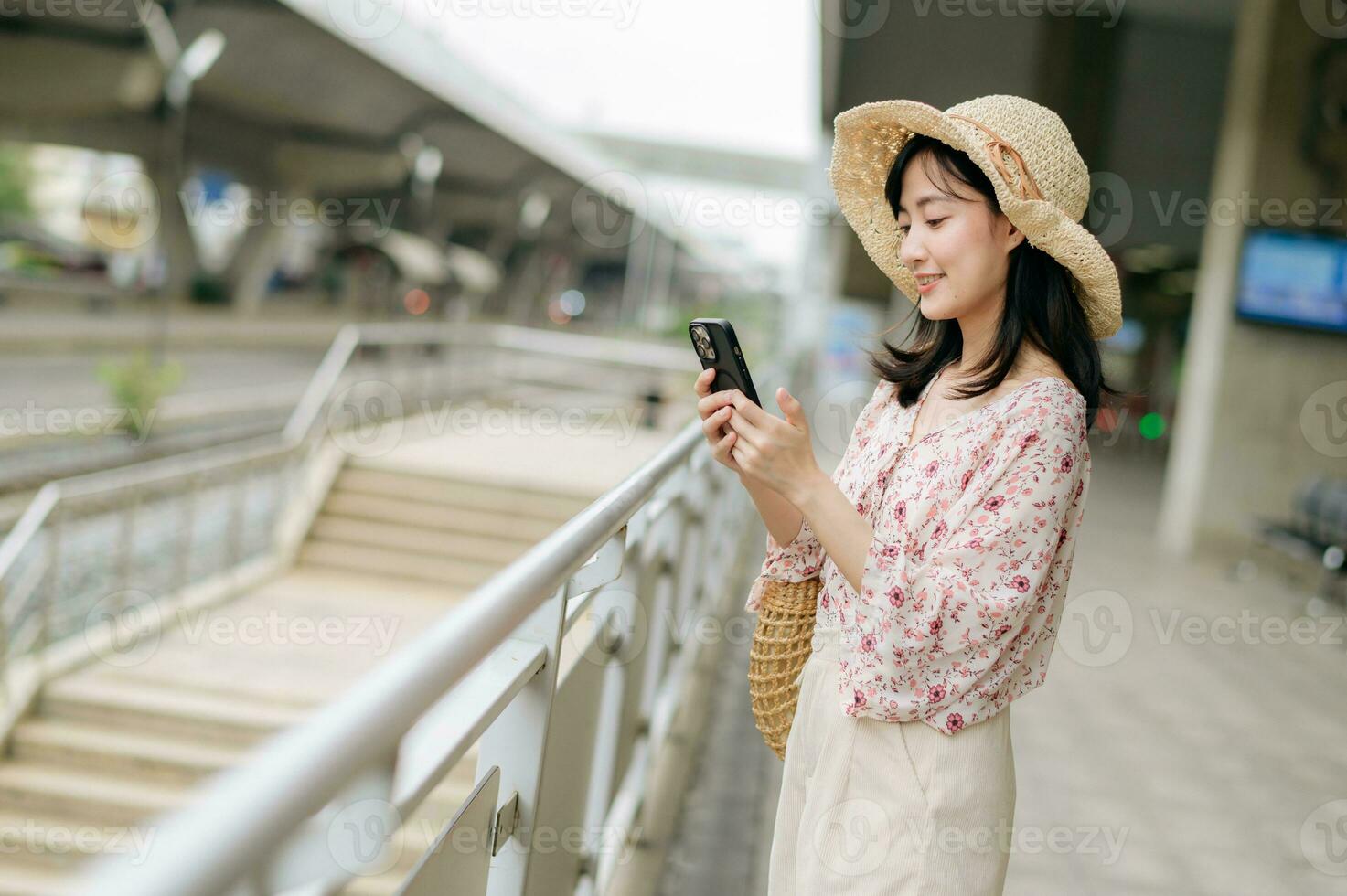 Asian young woman traveler with weaving basket using a mobile phone beside railway train station in Bangkok. Journey trip lifestyle, world travel explorer or Asia summer tourism concept. photo