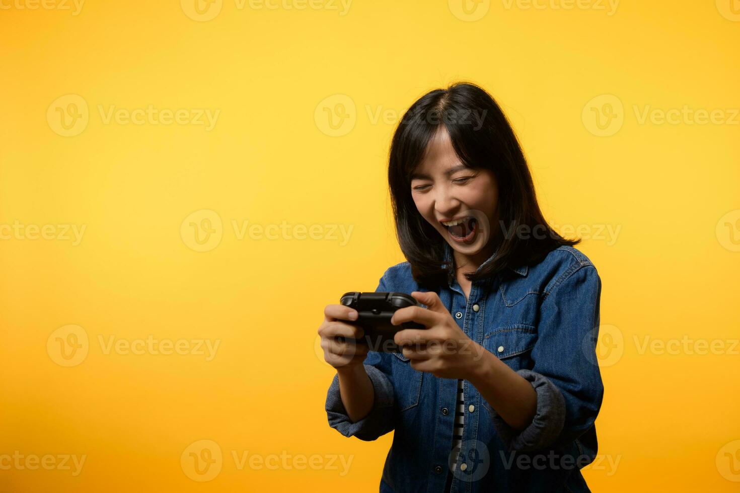 Portrait young asian woman with happy success smile wearing denim clothes holding joystick controller and playing video game. Fun and relax hobby entertainment lifestyle concept. photo