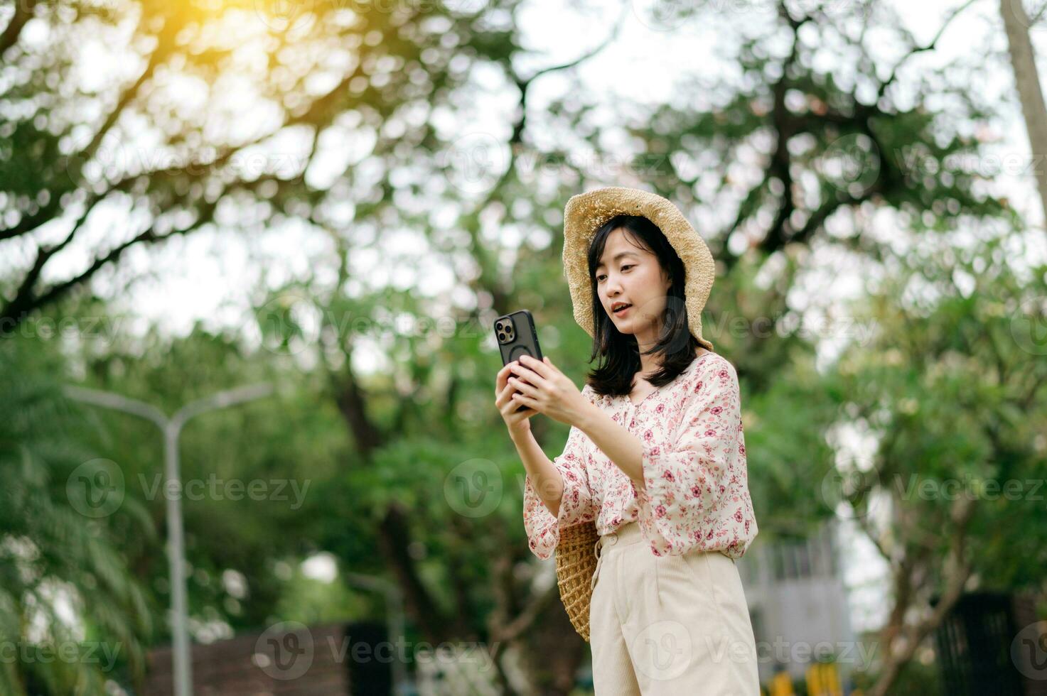 Portrait of asian young woman traveler with weaving hat and basket using mobile phone on green park nature background. Journey trip lifestyle, world travel explorer or Asia summer tourism concept. photo