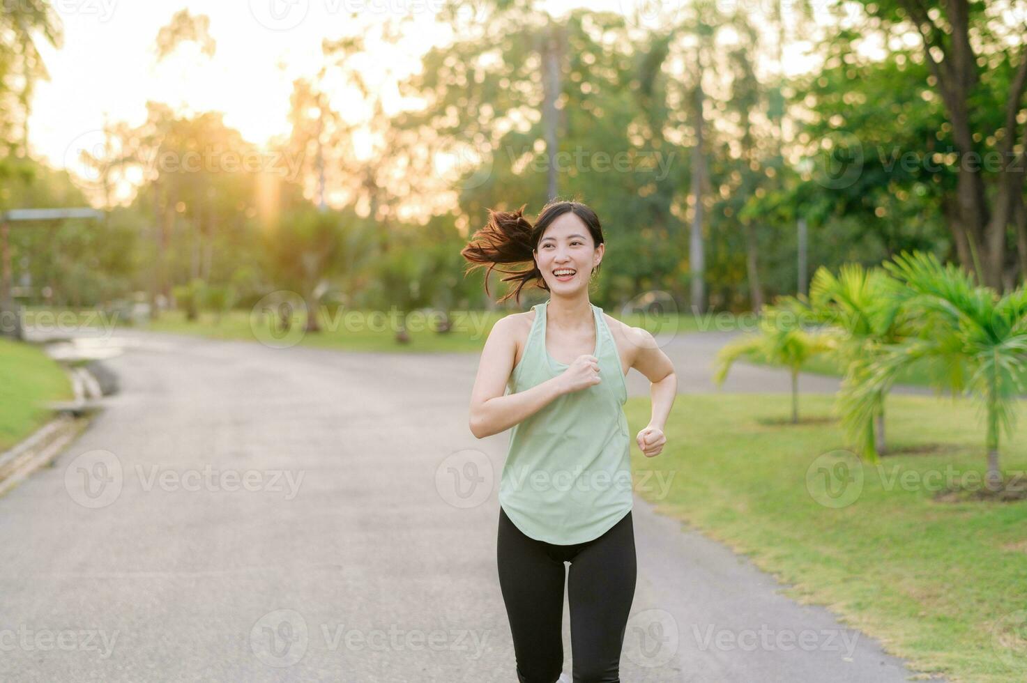 Fit Asian young woman jogging in park smiling happy running and enjoying a healthy outdoor lifestyle. Female jogger. Fitness runner girl in public park. healthy lifestyle and wellness being concept photo