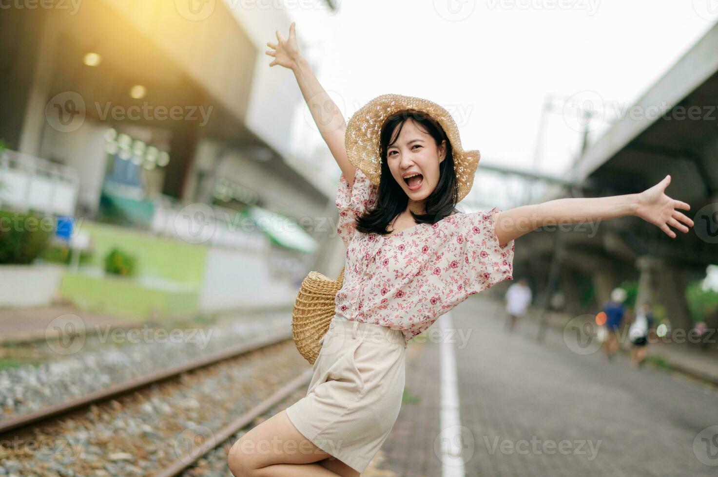joven asiático mujer viajero con Costura cesta contento sonriente mirando a un cámara junto a tren ferrocarril. viaje viaje estilo de vida, mundo viaje explorador o Asia verano turismo concepto. foto