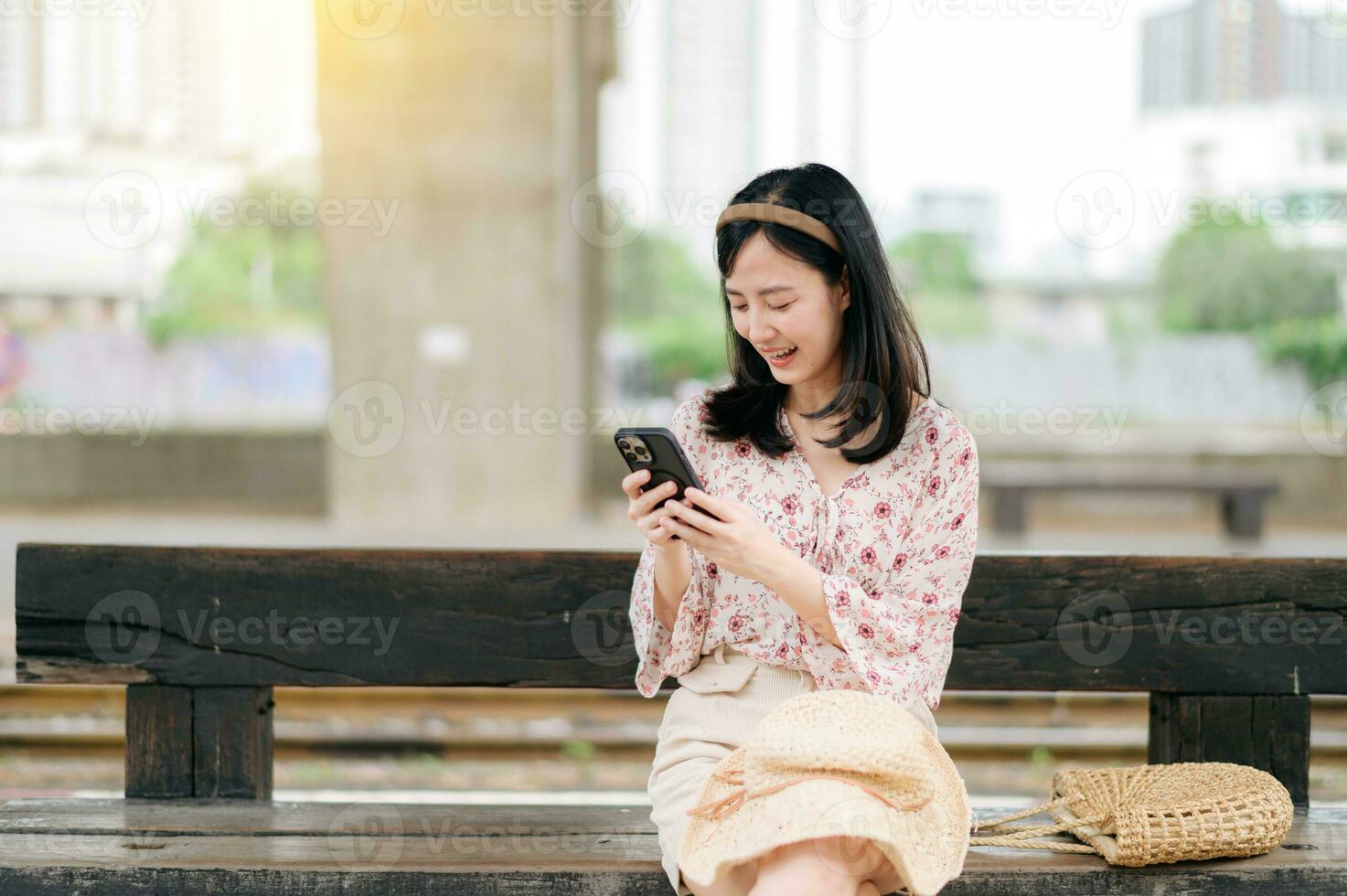 young asian woman traveler with weaving basket using a mobile phone and waiting for train in train station. Journey trip lifestyle, world travel explorer or Asia summer tourism concept. photo