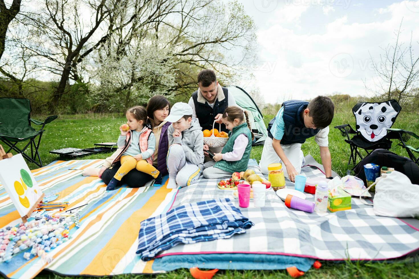 Happy young large family with four children having fun and enjoying outdoor on picnic blanket at garden spring park, relaxation. photo