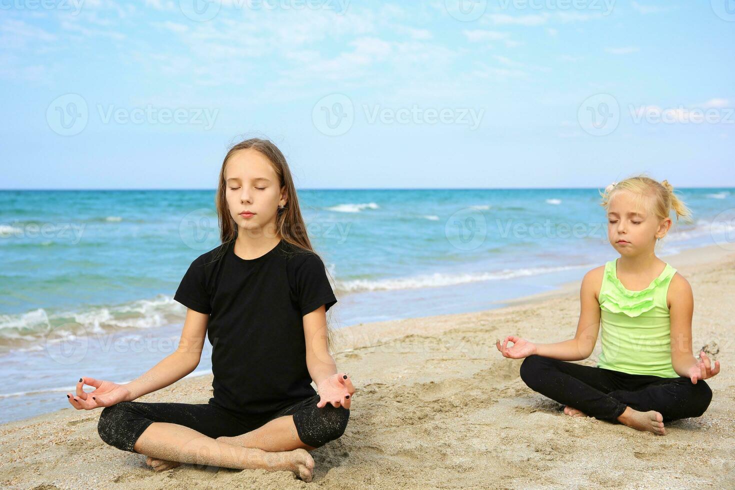 Girls practicing yoga on beach. Children are sitting in lotus position. photo