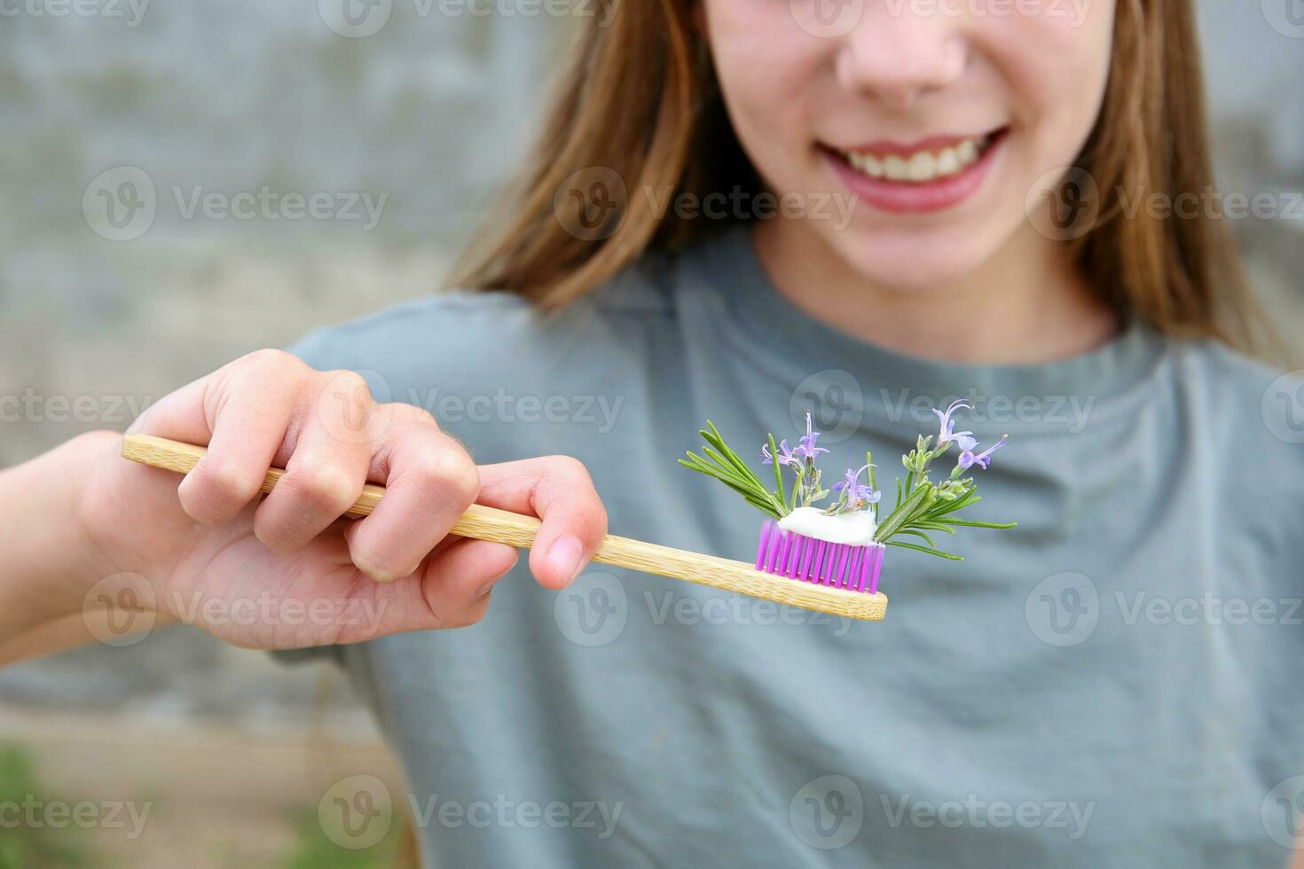 The girl holds a toothbrush with herbed toothpaste with rosemary in her hand. Selective focus on toothbrush and rosemary. photo