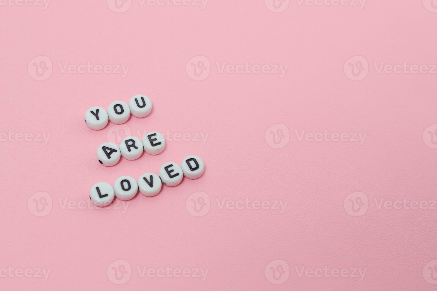 Top view of you are loved quotes made out of beads on pink background. motivation and success concept photo