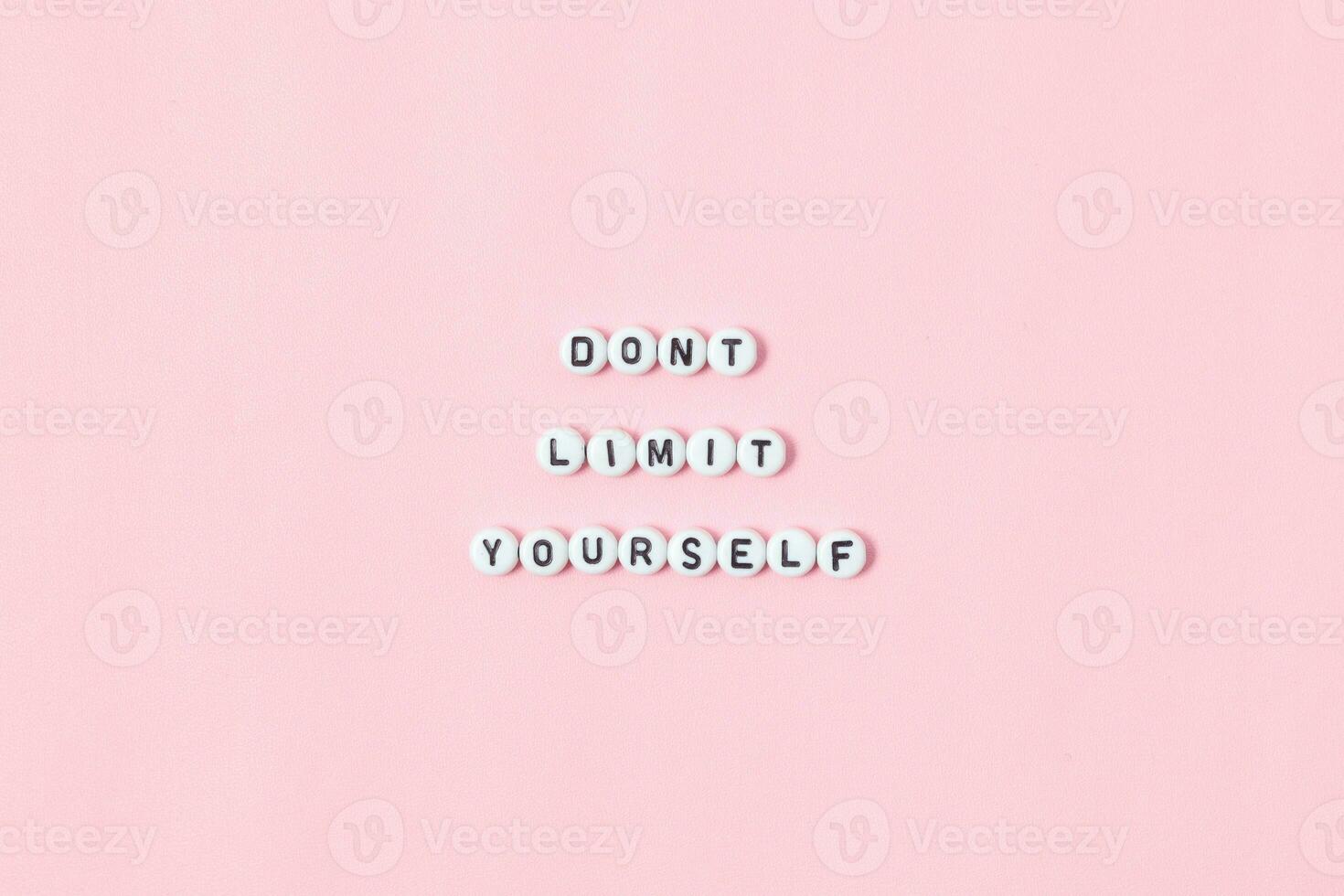 Top view of don't limit yourself quotes made out of beads on pink background. motivation and success concept photo