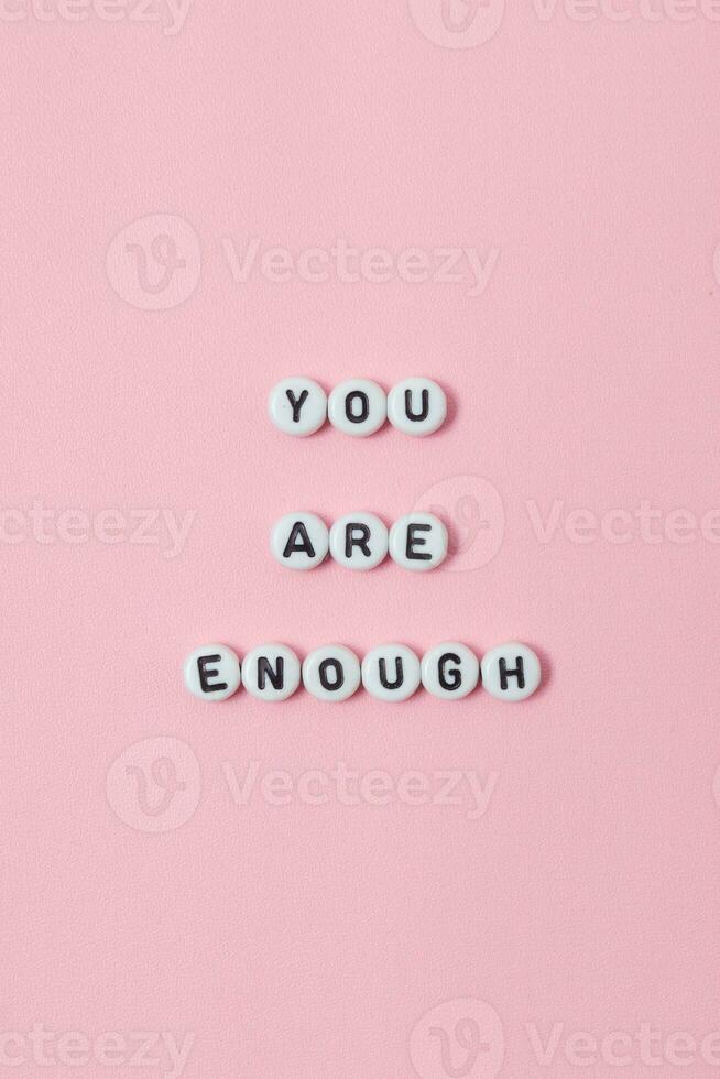 Top view of you are enough quotes made out of beads on pastel background. motivation and success concept photo