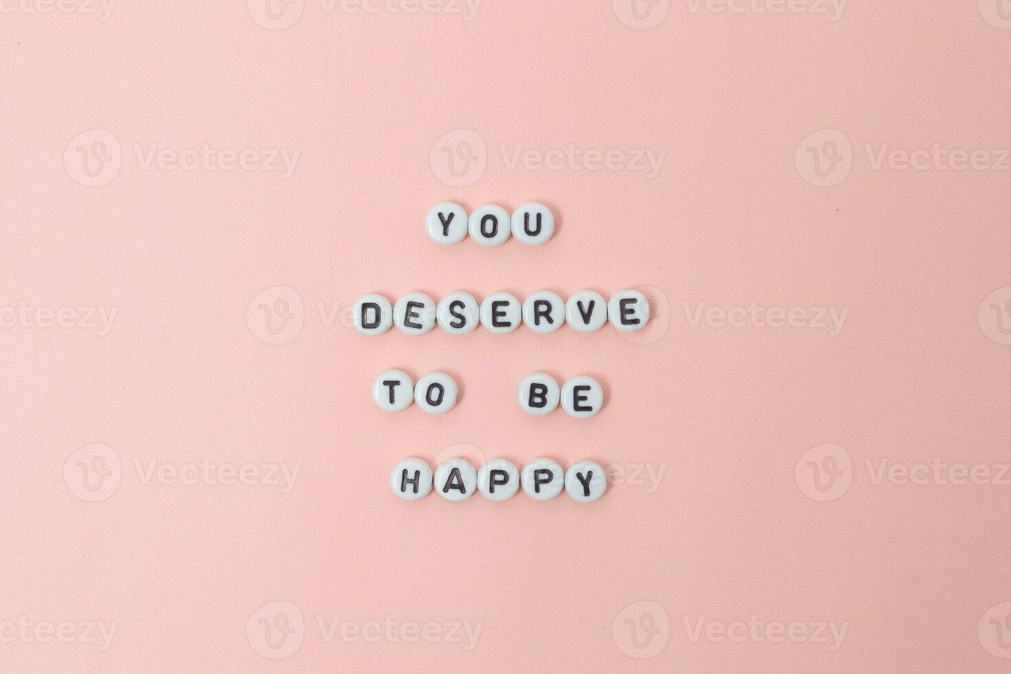 Top view of you deserve to be happy quotes made out of beads on pink background. motivation and success concept photo