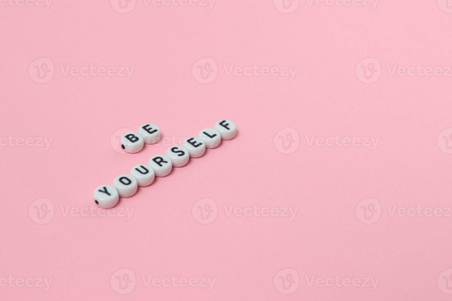 Top view of be yourself quotes made out of beads on pink background. motivation and success concept photo
