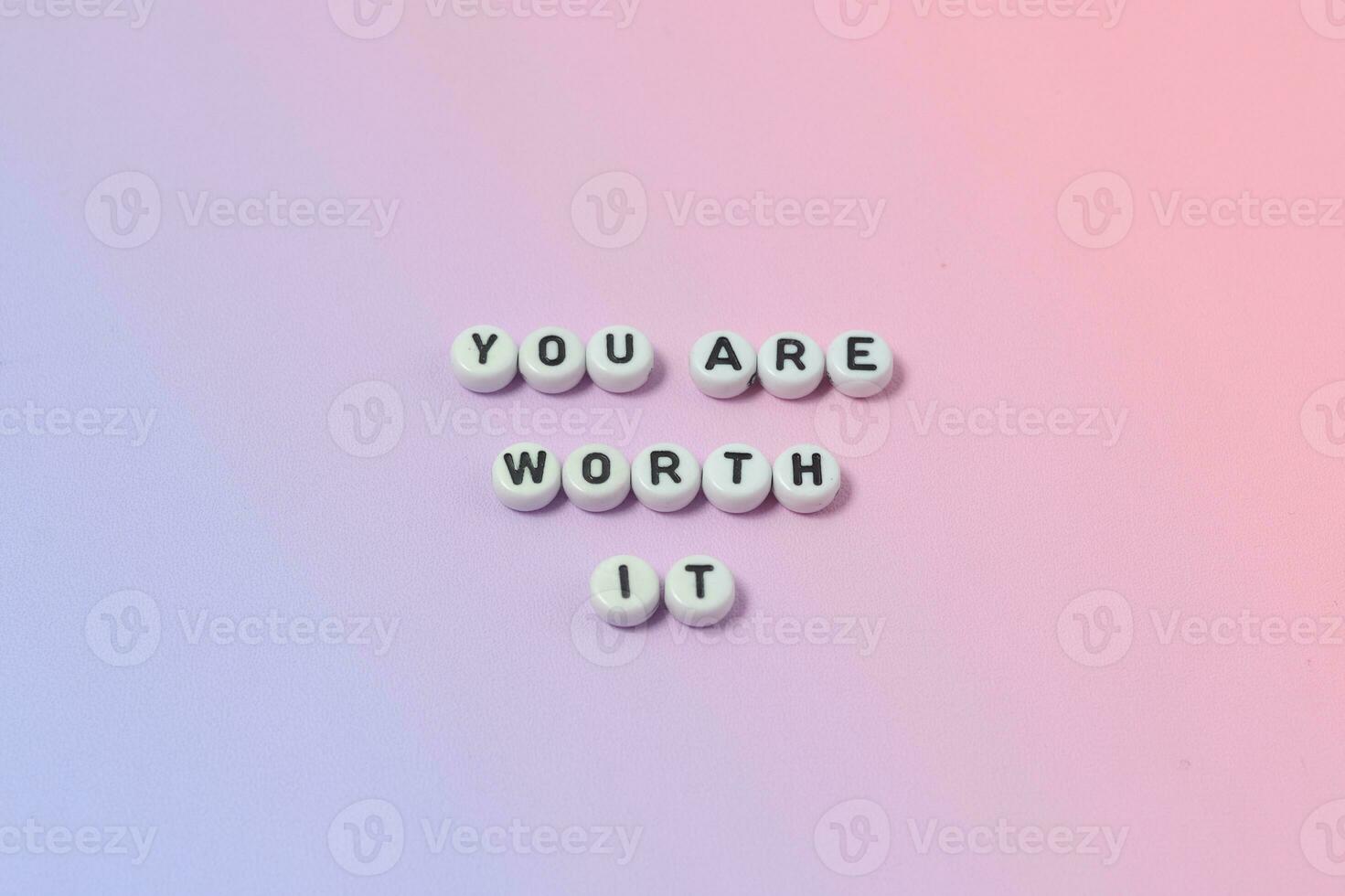 Top view of you are worth it quotes made out of beads on pastel background. motivation and success concept photo