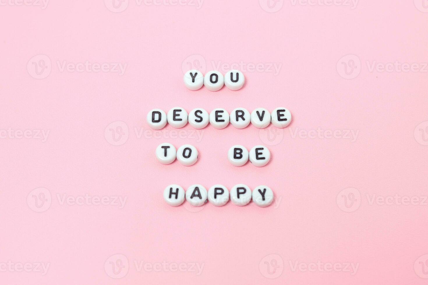 Top view of you deserve to be happy quotes made out of beads on pink background. motivation and success concept photo
