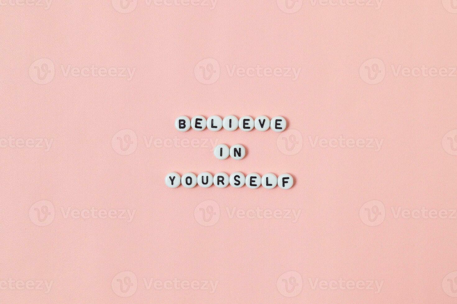 Top view of believe in yourself quotes made out of beads on pink background. motivation and success concept photo