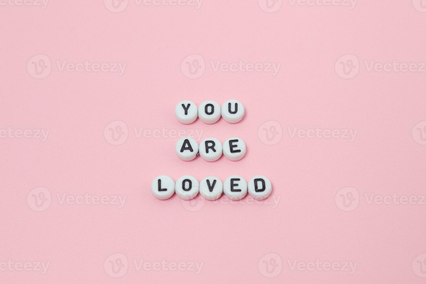 Top view of you are loved quotes made out of beads on pink background. motivation and success concept photo
