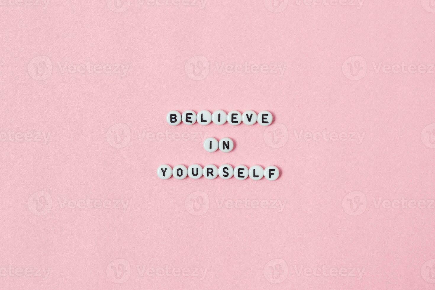 Top view of believe in yourself quotes made out of beads on pink background. motivation and success concept photo