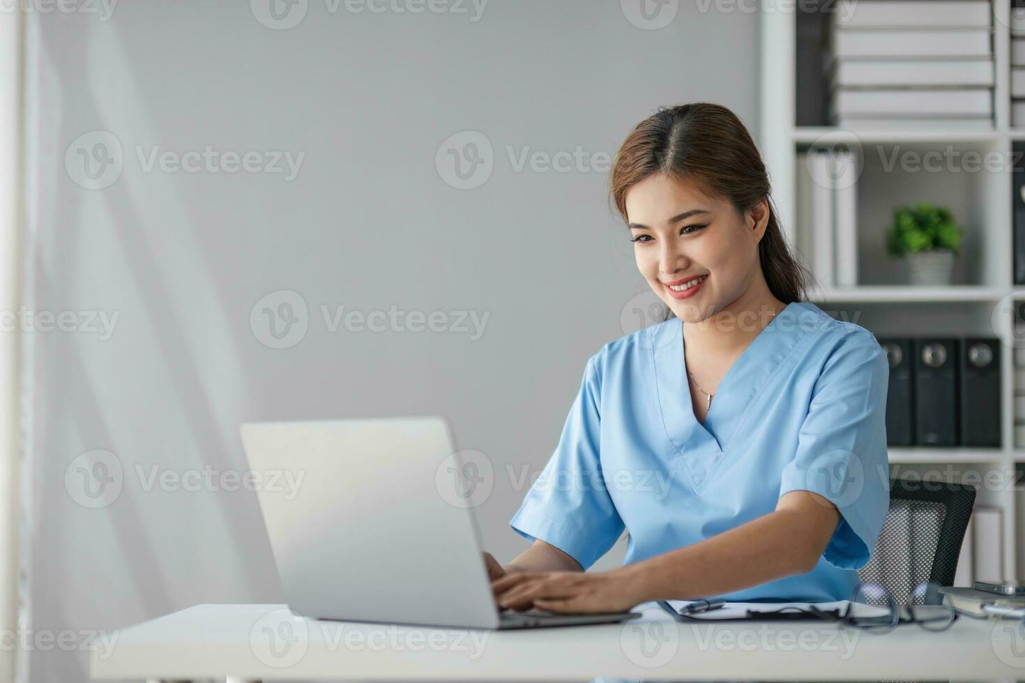 Asian doctor young beautiful woman smiling using working with a laptop computer and her writing something on paperwork or clipboard white paper at hospital desk office, Healthcare medical concept photo