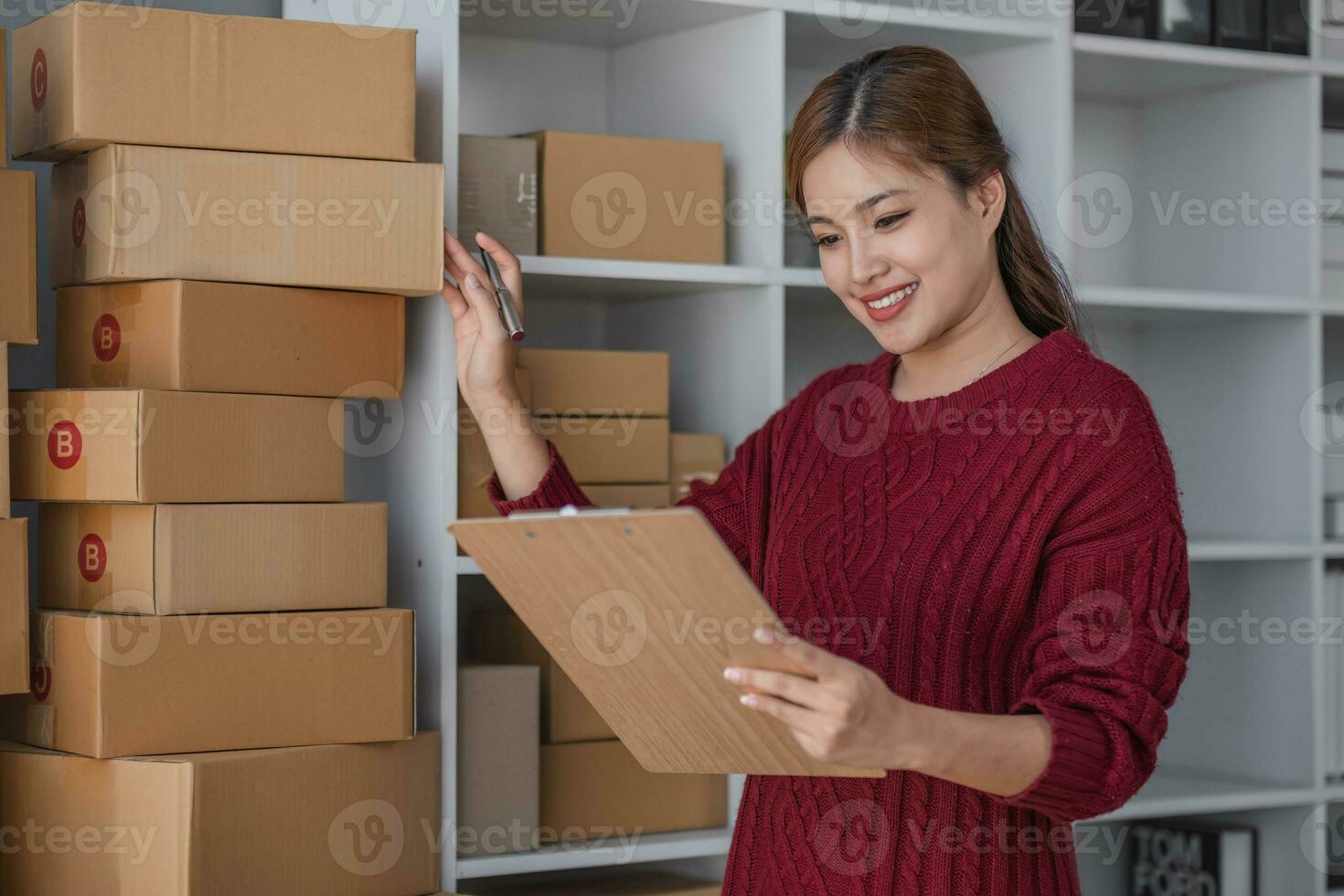 Starting small business entrepreneur of independent Asian woman smiling using computer laptop with cheerful success of online marketing package box items and SME delivery concept photo