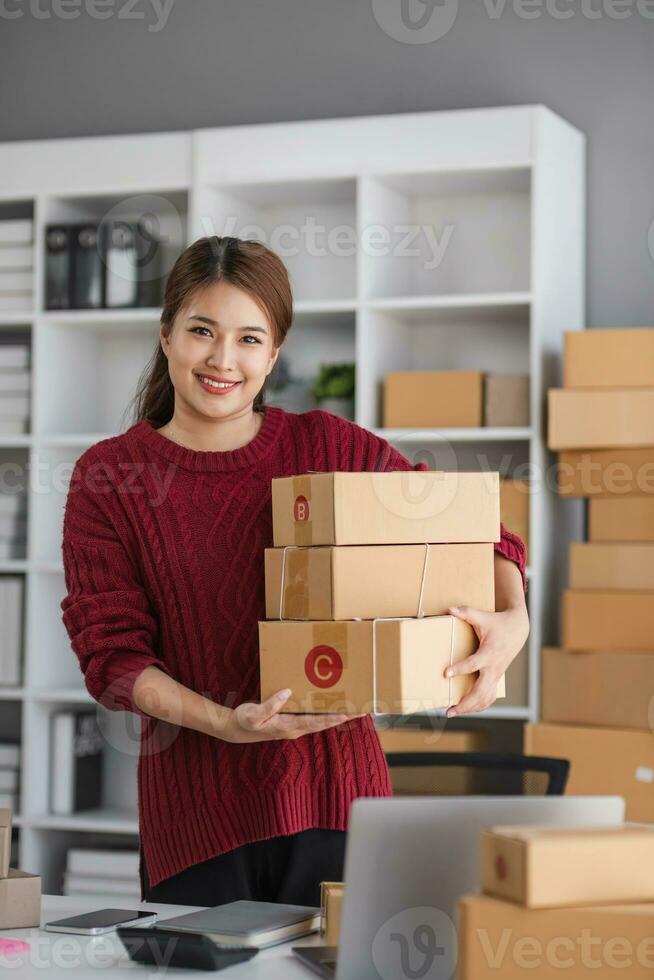 Starting small business entrepreneur of independent Asian woman smiling using computer laptop with cheerful success of online marketing package box items and SME delivery concept photo