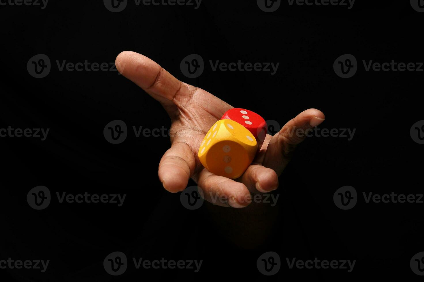 Asian male dark skinned single hand fist finger on black background holding wooden red yellow playing dice photo