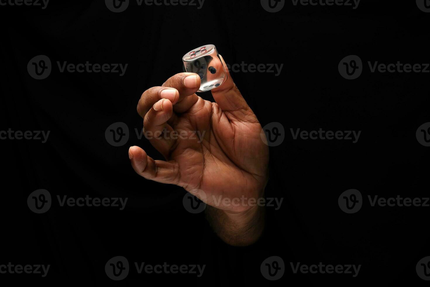 Asian male dark skinned single hand fist finger on black background holding transparent acrylic plastic playing dice photo