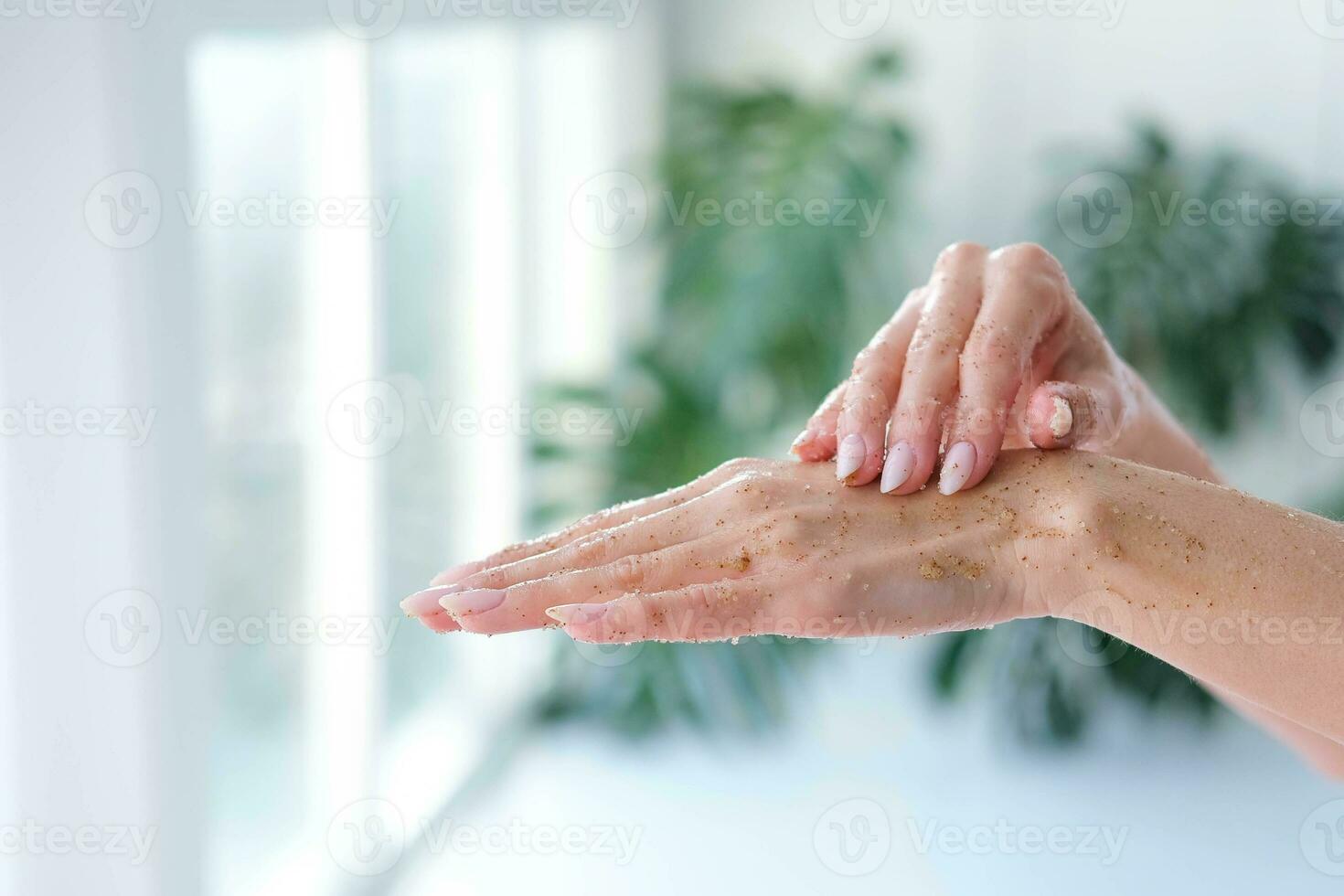 Close-up woman is hands with coffee massage scrub on monstera blurred background. Cosmetology, hand care, spa cosmetics, beauty concept. photo
