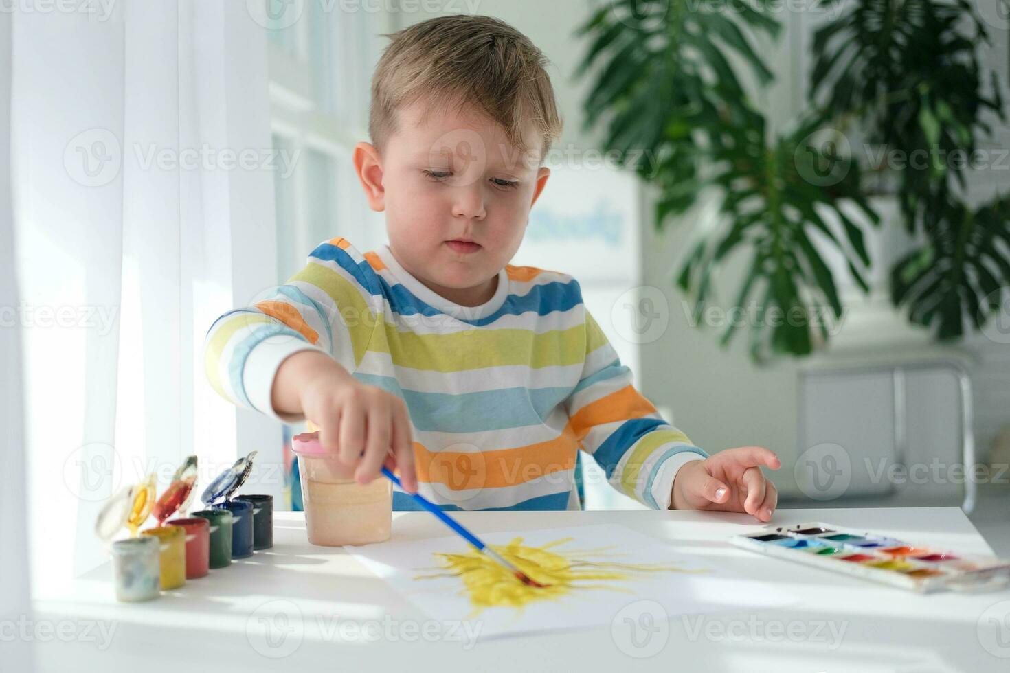 A little boy draws a picture with paints on a sheet of paper. The child is learning to draw. Home creativity. photo