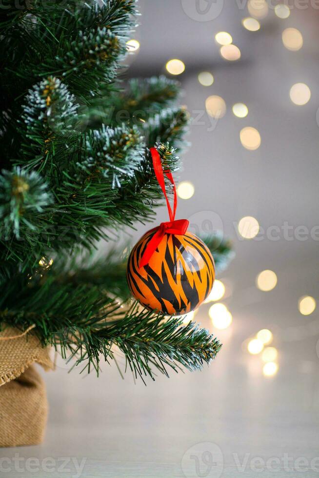 Christmas ball painted as tiger stripes spins on blurred christmas garland. background.  2022 is a year of the Tiger. Happy New Year . Symbol of year lunar chinese calendar tiger on Christmas  ball . photo