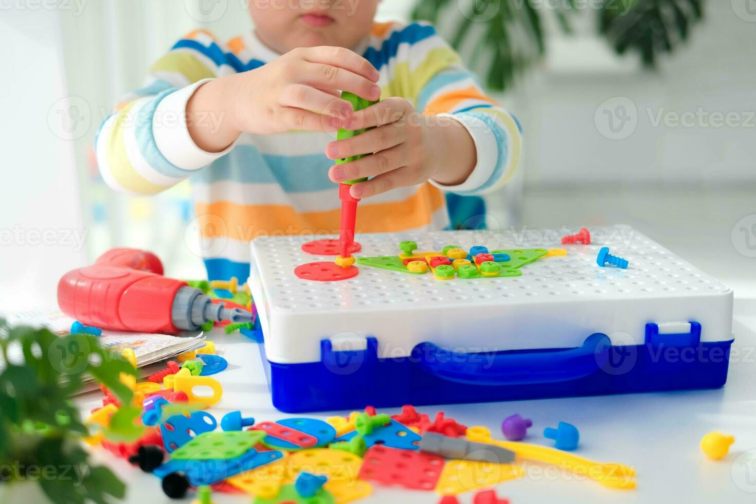 Little boy playing set with a screwdriver and a drill,  and screws and parts . The child plays builder with a toy drill to develop imagination and motor skills. Educational logic toys for children. photo