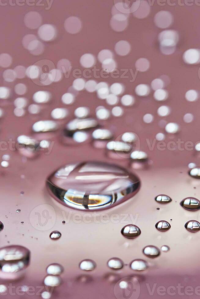 A large drop and splashes of micellar water on a pink background. photo