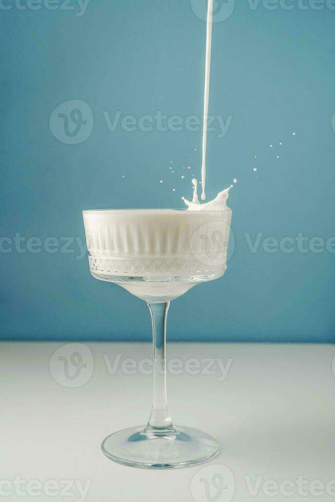 Milk pours into a beautiful crystal glass on a blue background and splashes around. photo