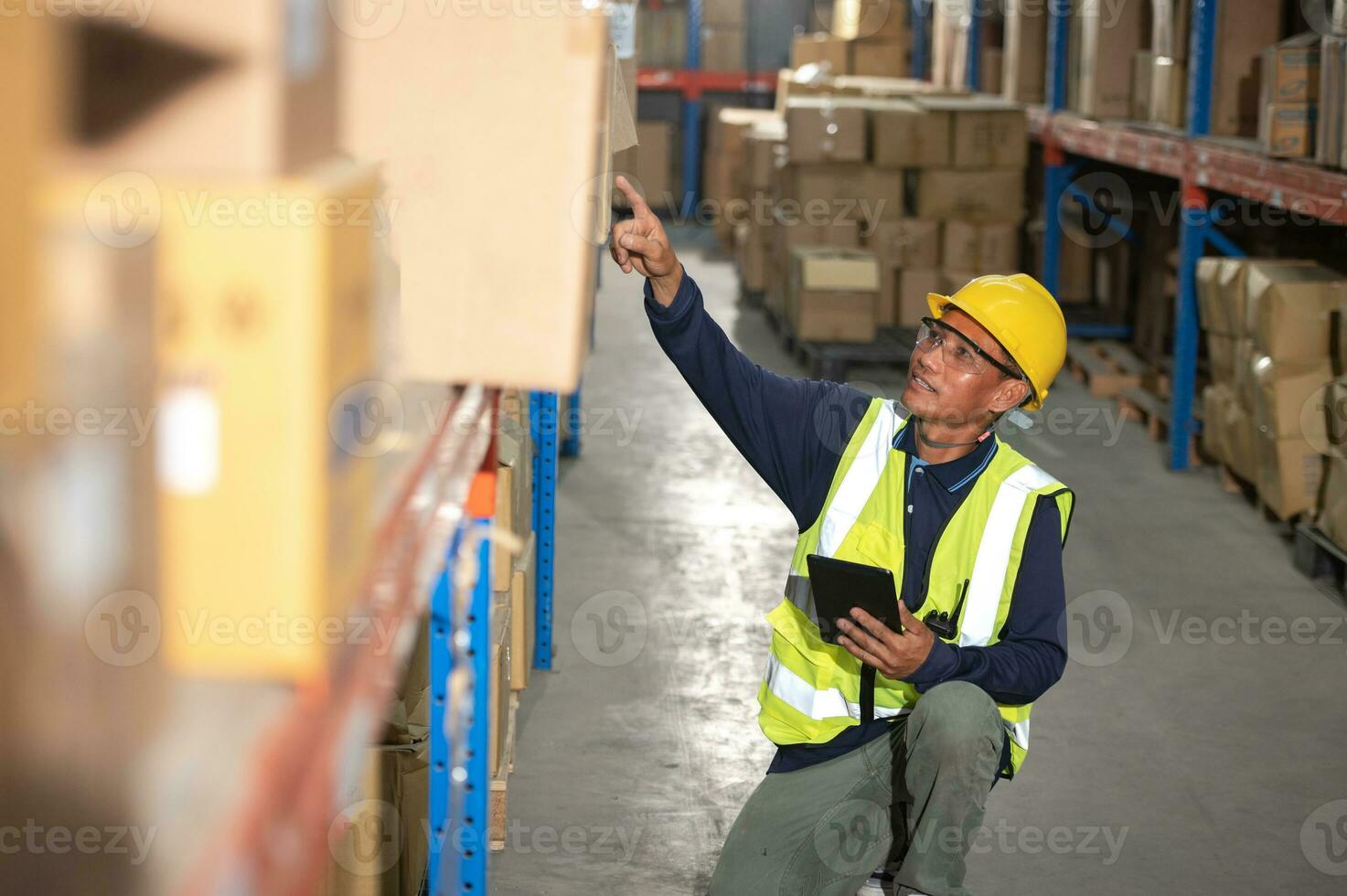 Asian warehouse factory male manager happy using digital tablet communication tools In a warehouse while standing on a shelf looking at the camera photo
