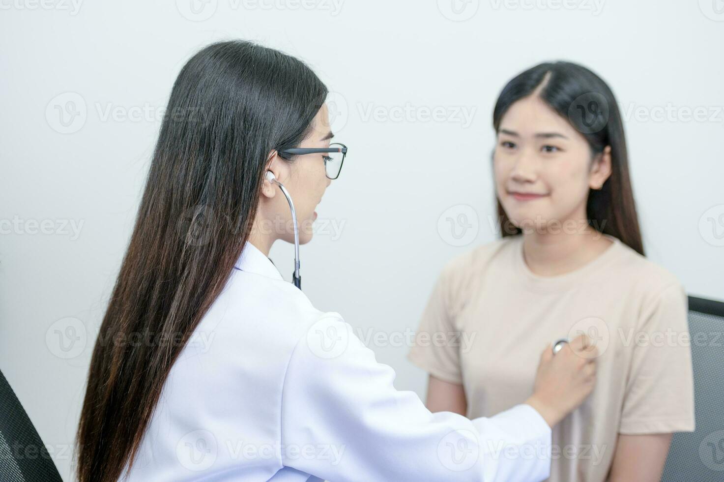 Asian female doctor in uniform holding a stethoscope and using it to measure the heart rate of an asian female patient with heart disease photo