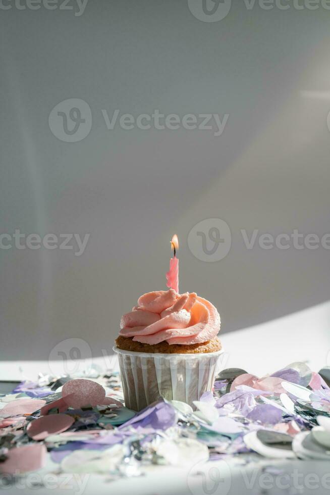 A cupcake with a candle stands on a white background with a shadow. photo