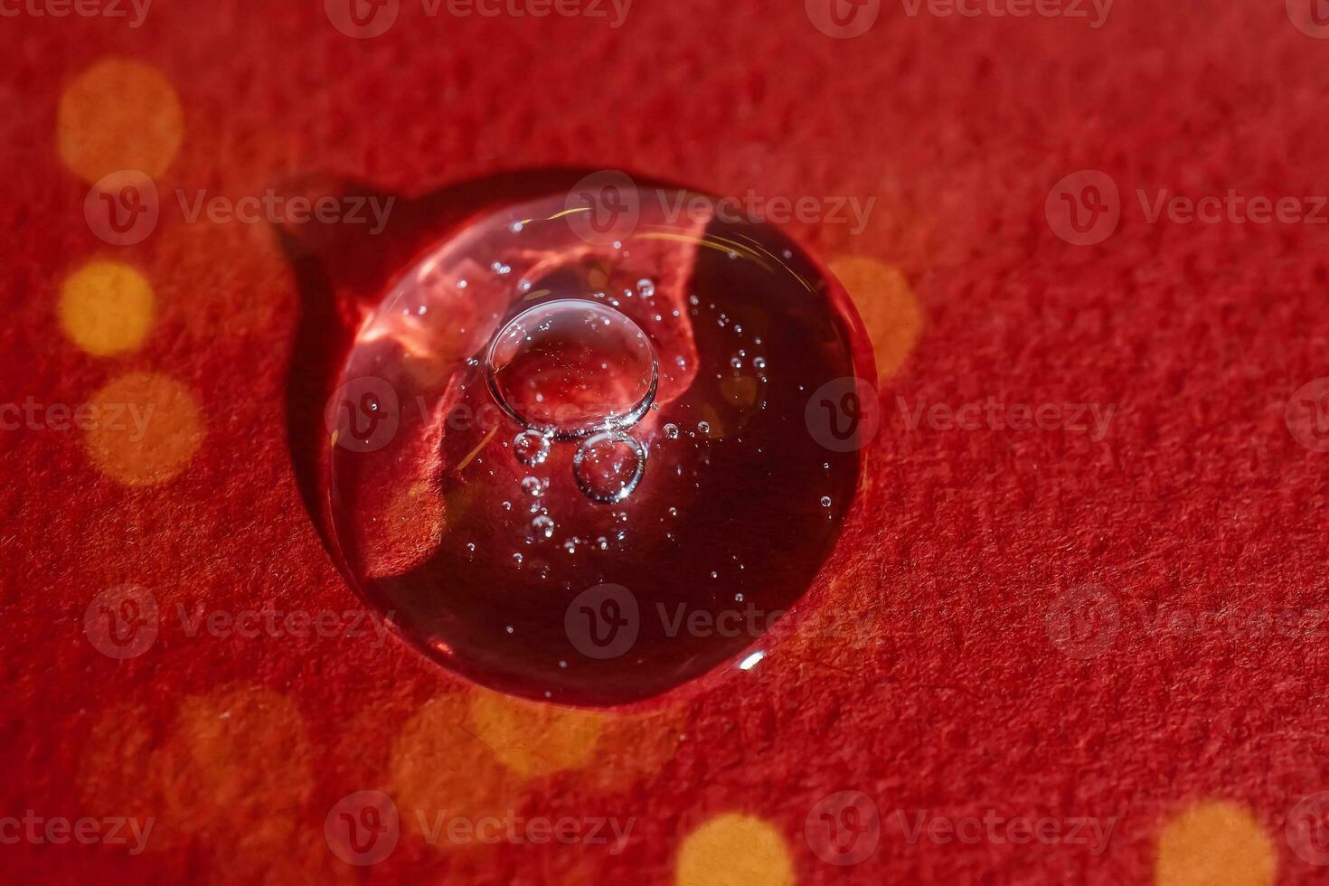 A drop of serum on a red background with bokeh. photo