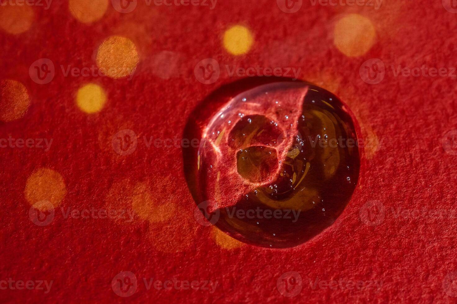 A drop of serum on a red background with bokeh. photo