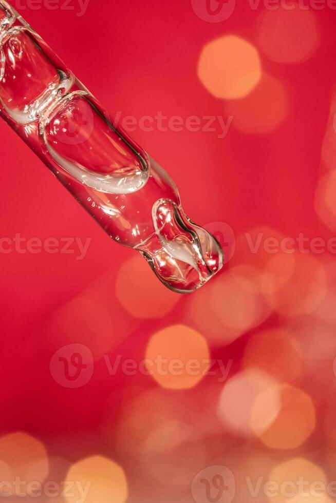 Pipette with serum on a red holiday background with bokeh. photo