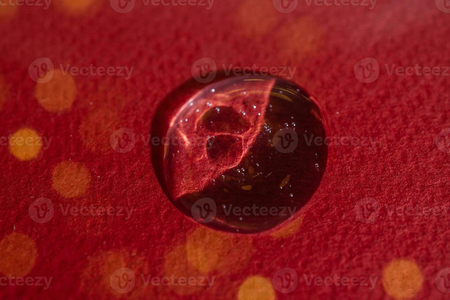 A drop of serum on a red background with bokeh. photo