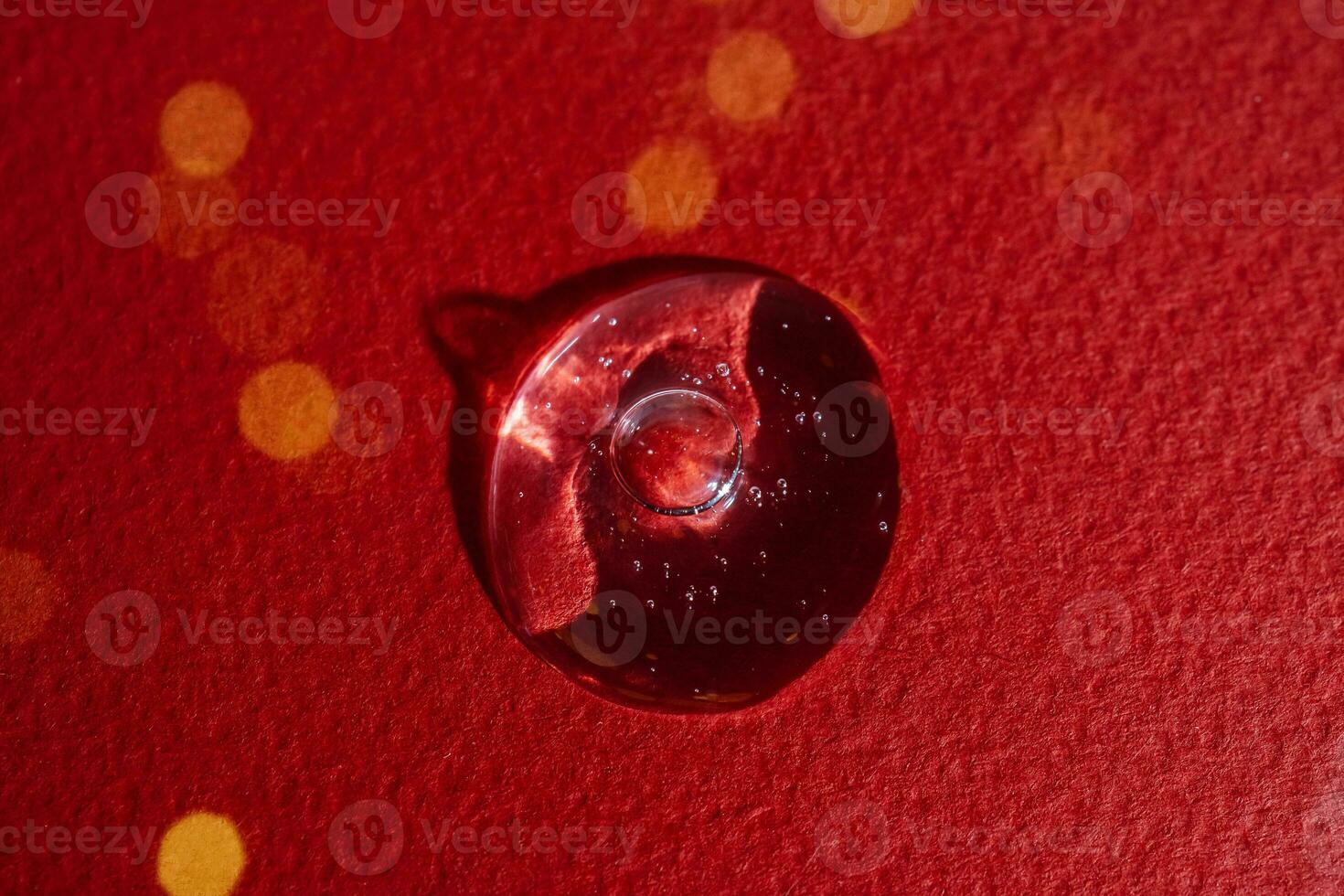 A drop of serum on a red background with bokeh. photo