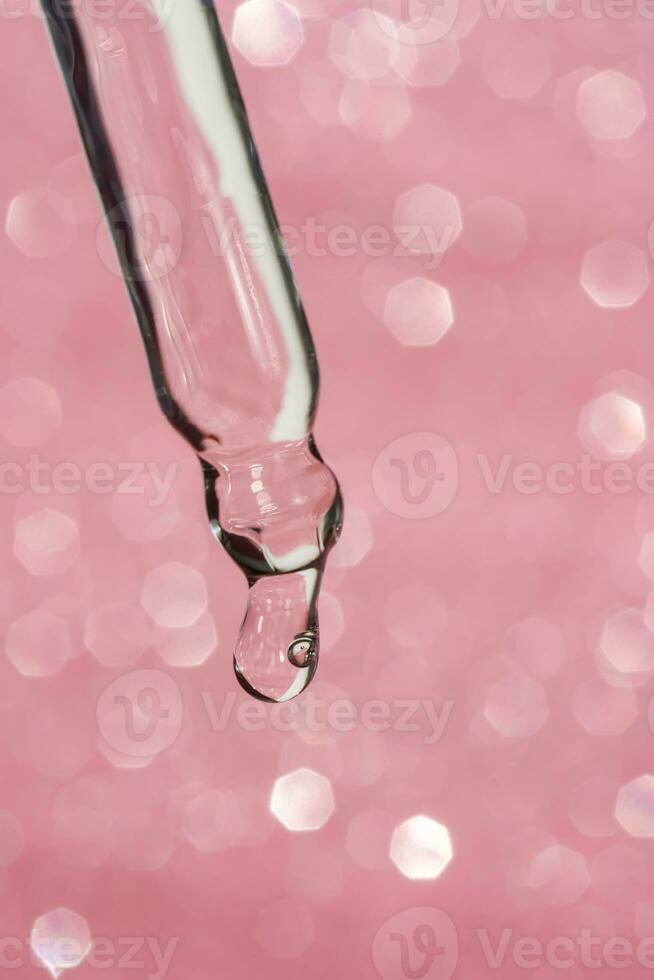 Cosmetic pipette with a drop on pink background. photo