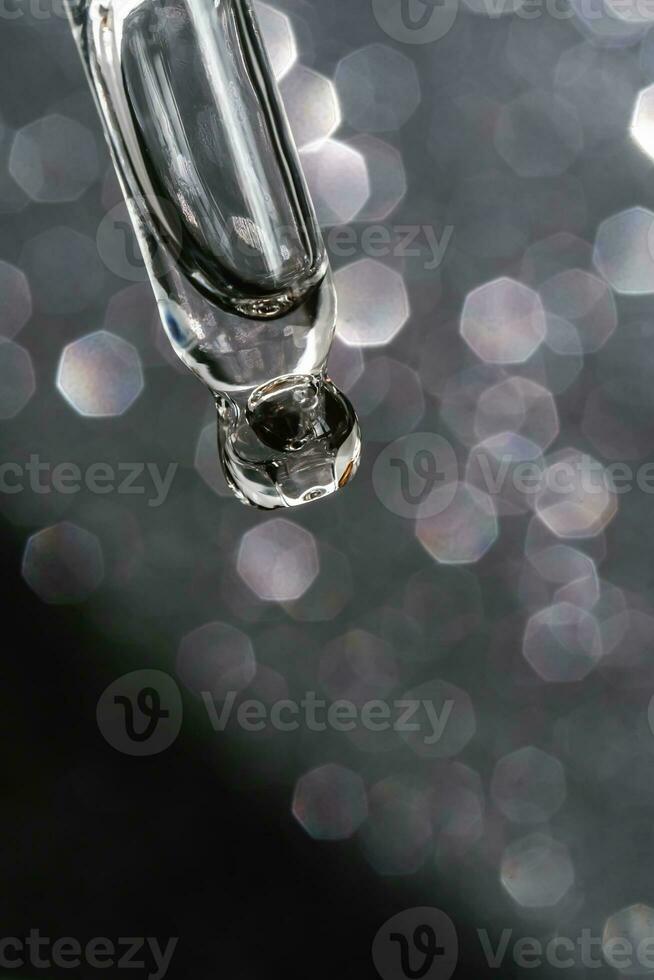 Cosmetic pipette with a drop on dark background. photo