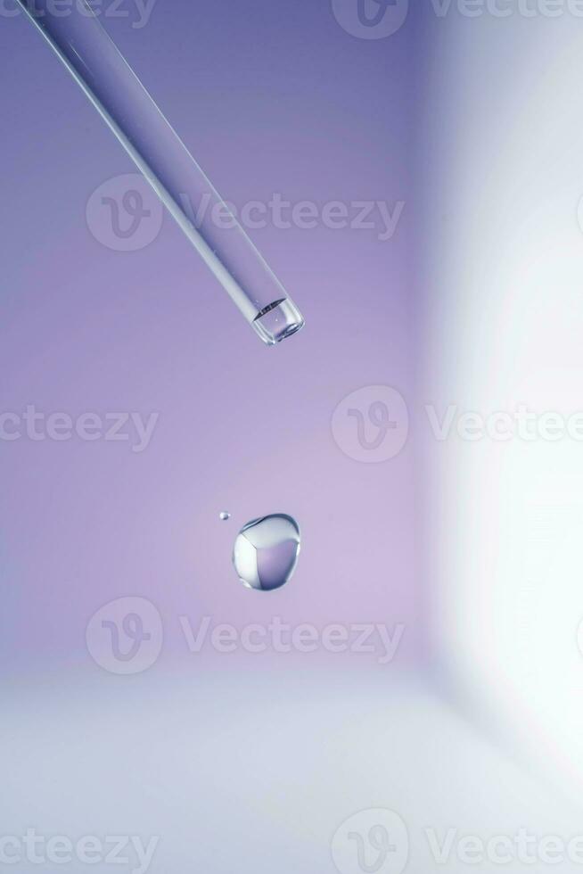 A drop of cosmetic oil falls from the pipette on a purple floral background. photo