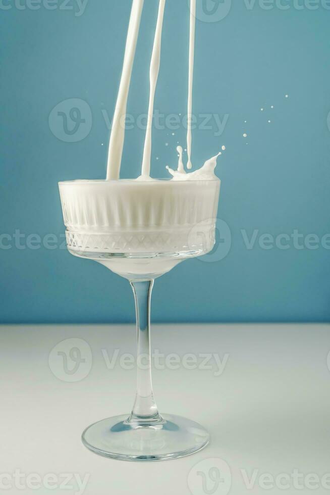 Milk pours into a beautiful crystal glass on a blue background and splashes around. photo