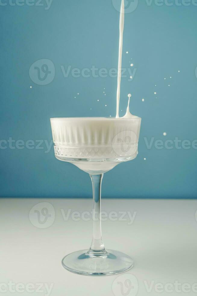 Milk pours into a beautiful crystal glass on a blue background and splashes around. photo