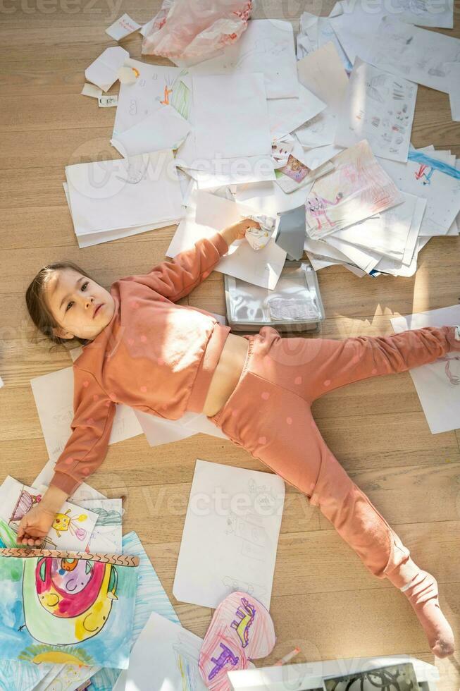 un niña entre el lío y dispersado hojas en el habitación. foto