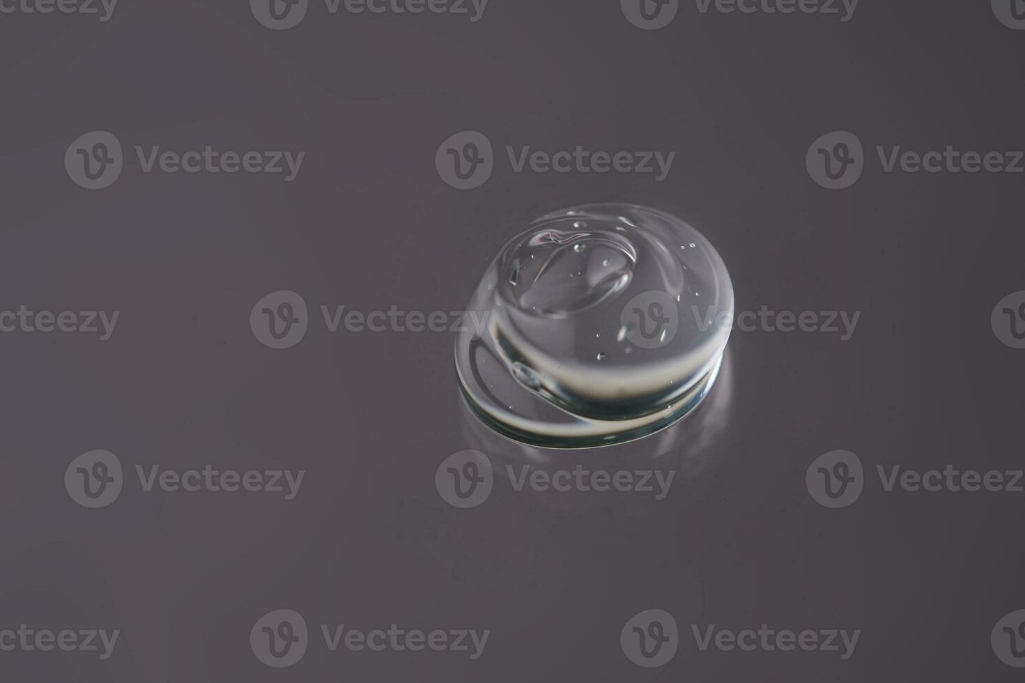 Drop of cosmetic transparent gel on a grey background. The texture of the serum, heir gel or hyaluronic booster. photo