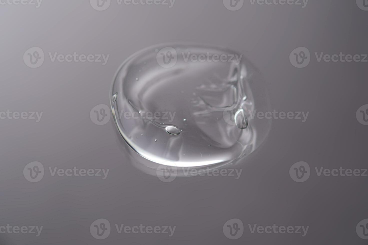 Drop of cosmetic transparent gel on a grey background. The texture of the serum, heir gel or hyaluronic booster. photo