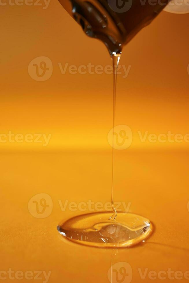 A drop of body gel or shampoo pouring from above on a yellow saturated background. photo